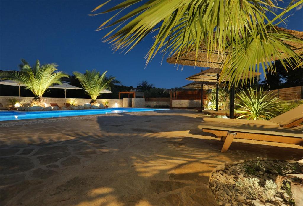 Evening view of illuminated outside pool and terrace with sun loungers and palms
