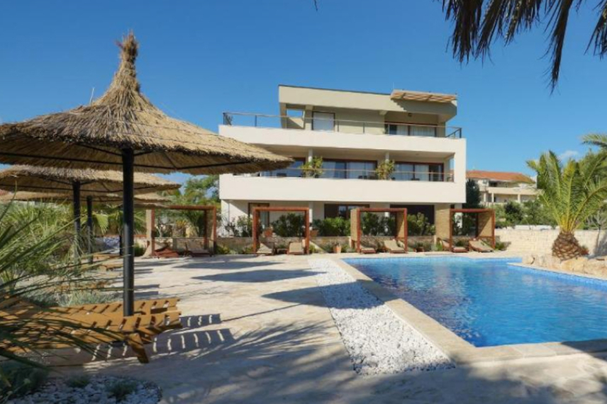 View of the sun covered Villa from across the yard with big outside pool and palms on the terrace